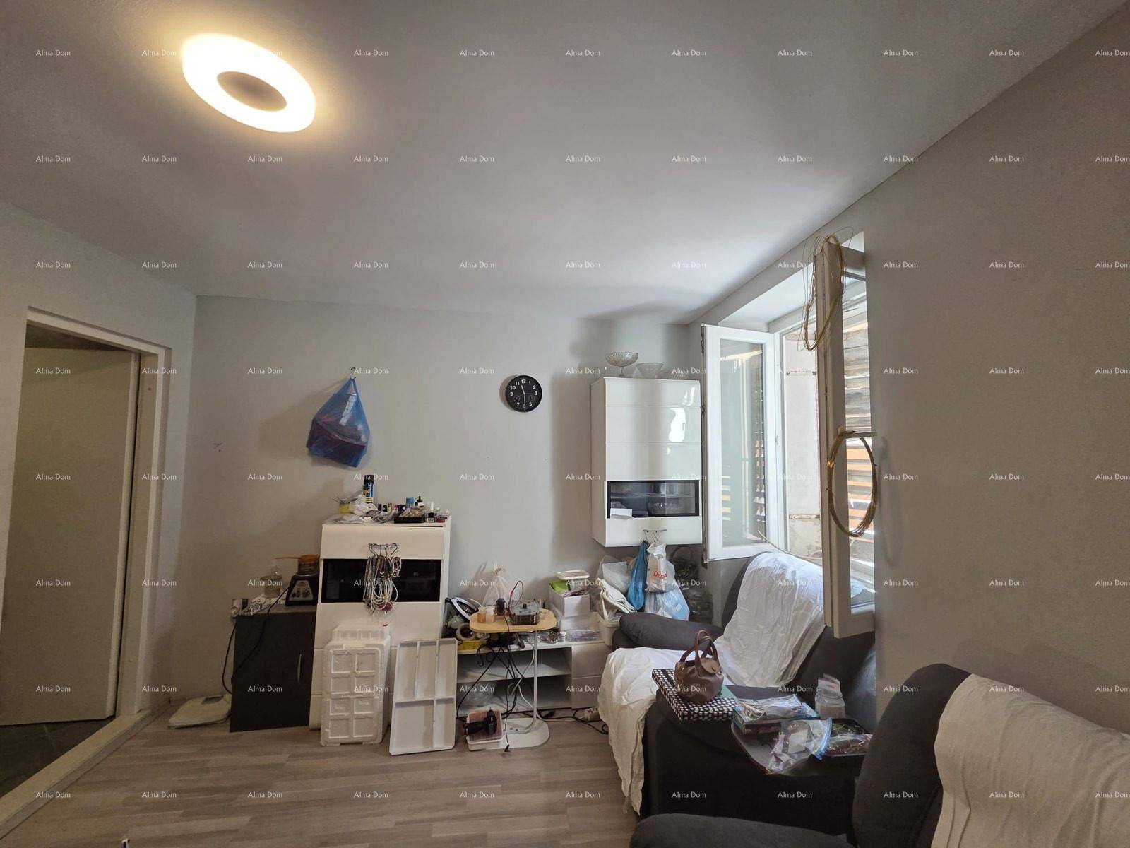 Helles Wohnzimmer mit Laminatboden, einem Fenster mit Fensterläden und einfacher Einrichtung.