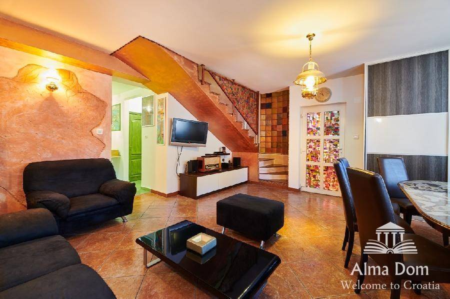 Heller Wohn- und Essbereich mit Esstisch, Sofa und Zugang zur Treppe auf Fliesenboden.