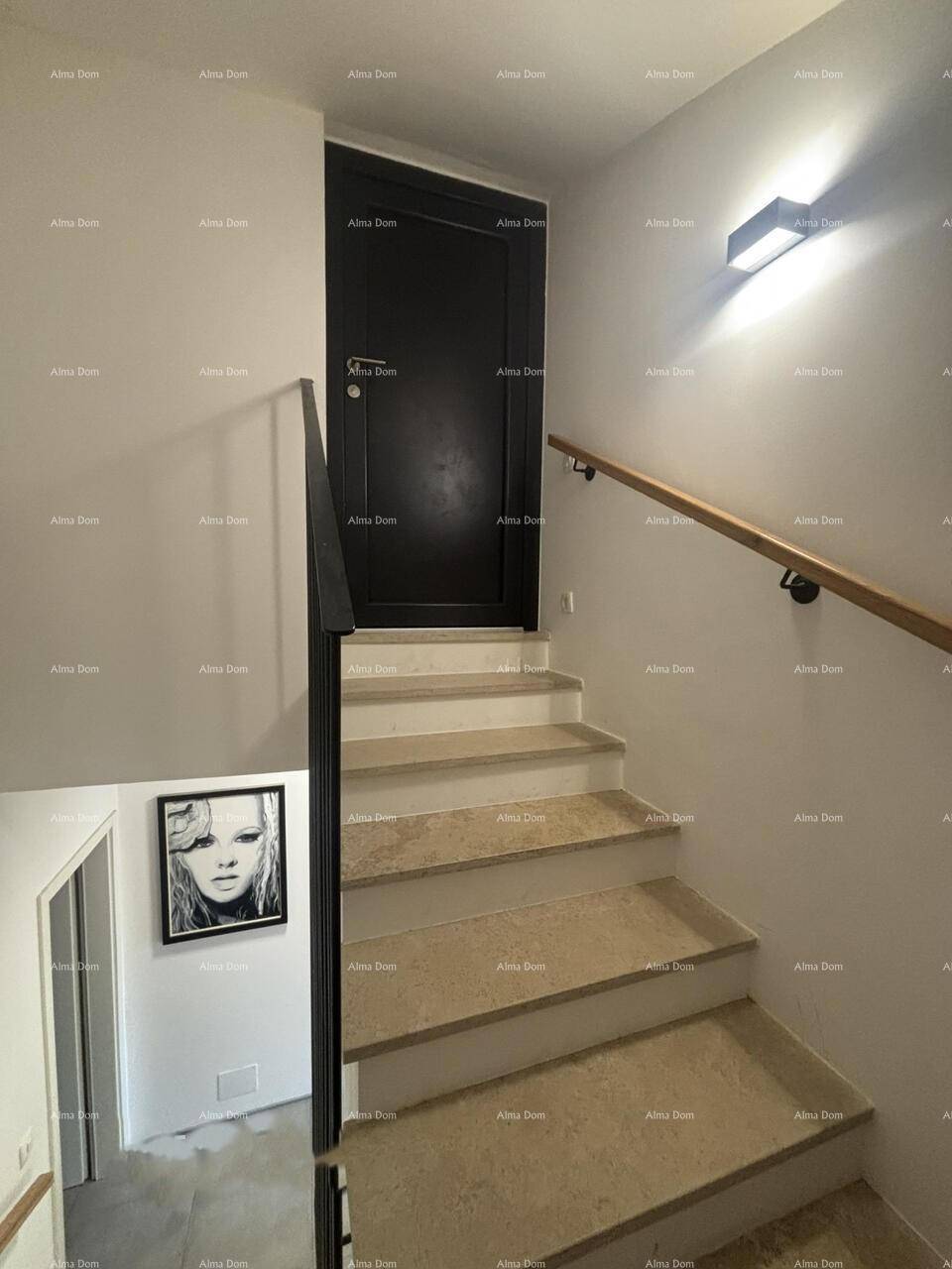 Treppenhaus mit Steinstufen, schwarzem Geländer und moderner Wandbeleuchtung.