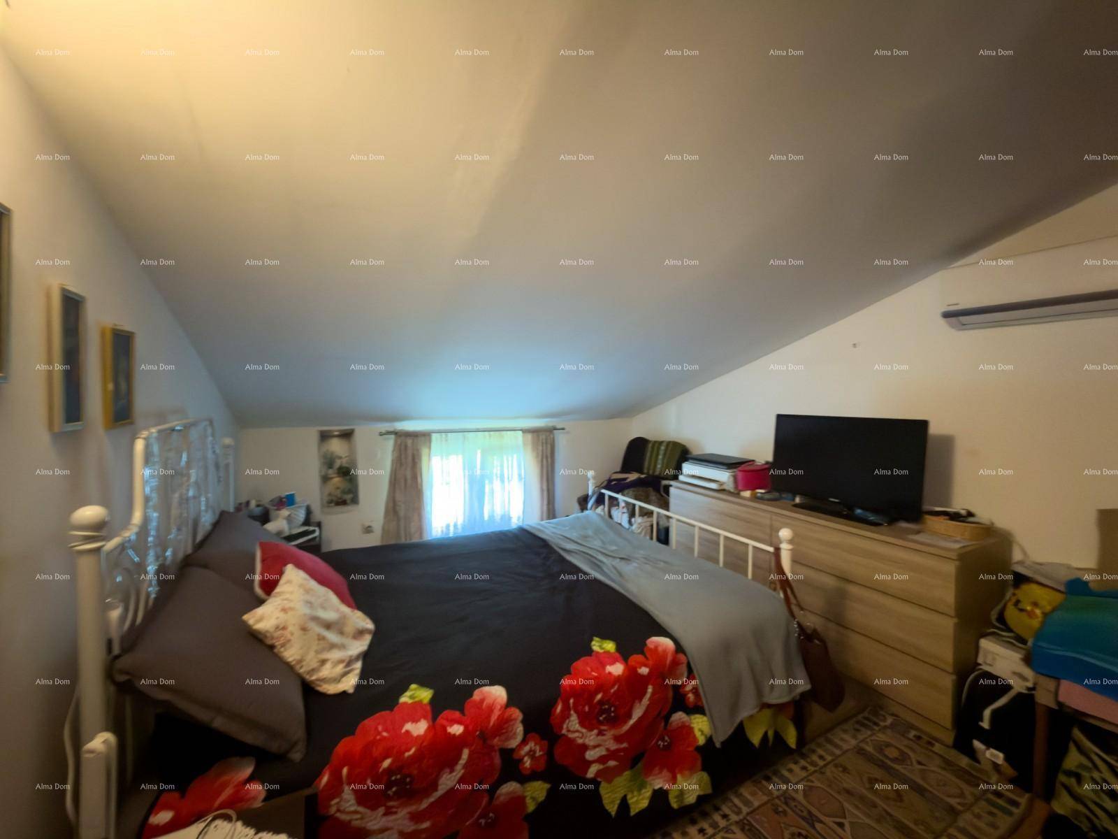 Schlafzimmer mit Doppelbett, Kommode, Fernseher und Klimaanlage unter einer Dachschräge.