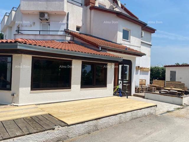 Gebäudefassade mit einer neuen Holzterrasse und traditionellem Ziegeldach unter klarem Himmel.
