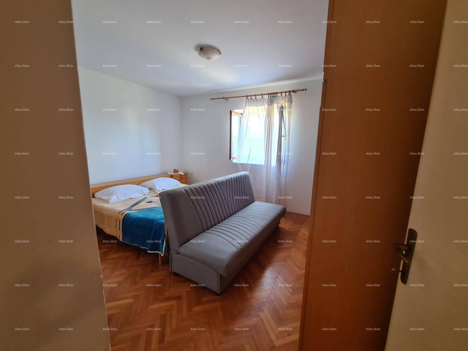 Schlafzimmer mit Bett, Schlafsofa und Holzparkettboden, durch eine Tür sichtbar.