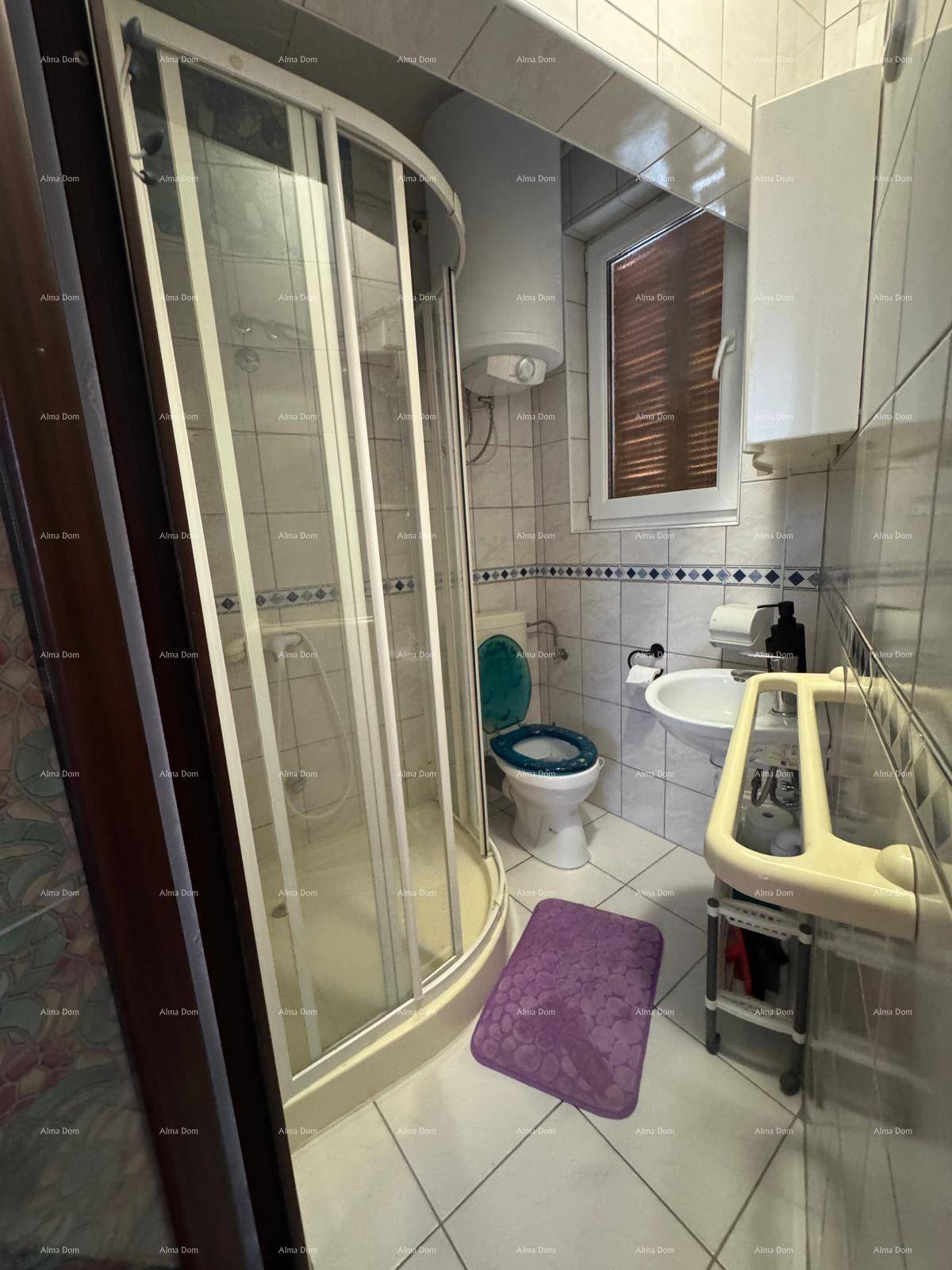 Kleines Badezimmer mit Duschkabine, WC, Waschbecken und Fenster, gefliest in Hellblau.