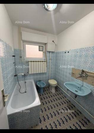 Badezimmer mit hellblauen Fliesen, Badewanne, WC, Bidet und Fenster mit Heizkörper.
