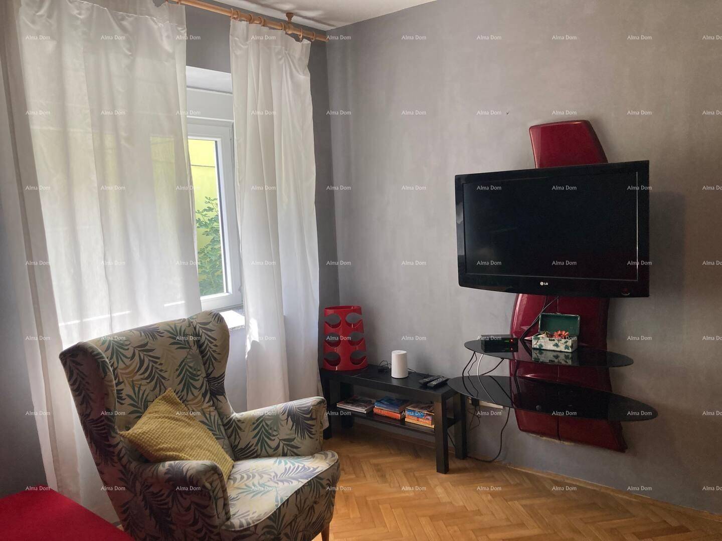Helles Wohnzimmer mit Fernseher an der Wand, einem Sessel und Parkettboden.