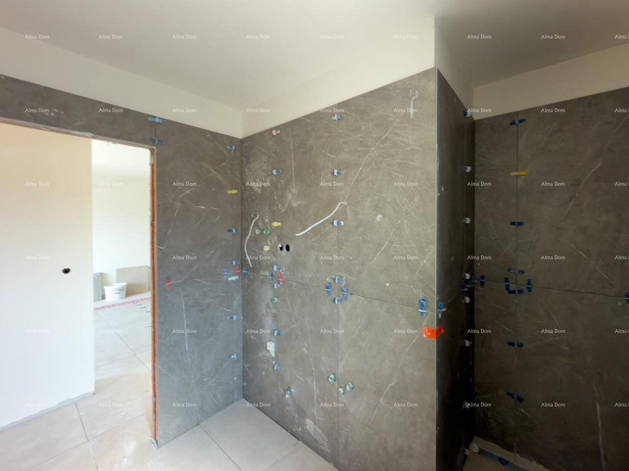 Badezimmer im Rohbau mit grauen Fliesen an den Wänden und einem angrenzenden Türrahmen.