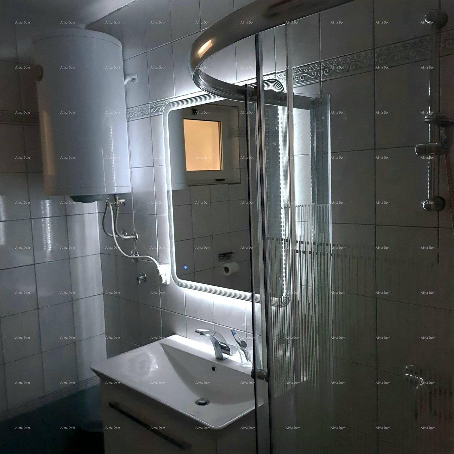 Badezimmer mit Duschkabine, beleuchtetem Spiegel und Boiler, in hellen Fliesen gehalten.