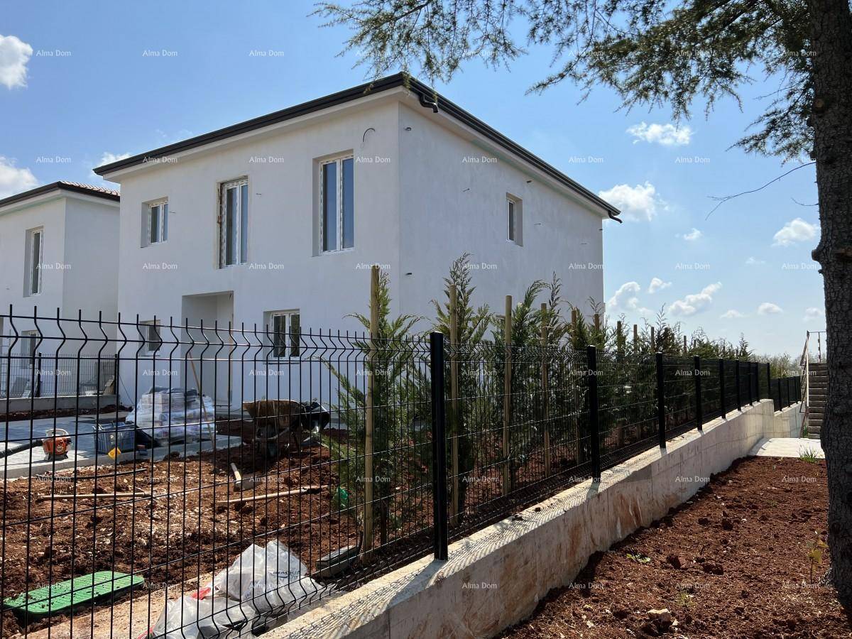 Seitenansicht eines modernen Neubaus mit weißer Fassade und junger Bepflanzung im Gartenbereich.