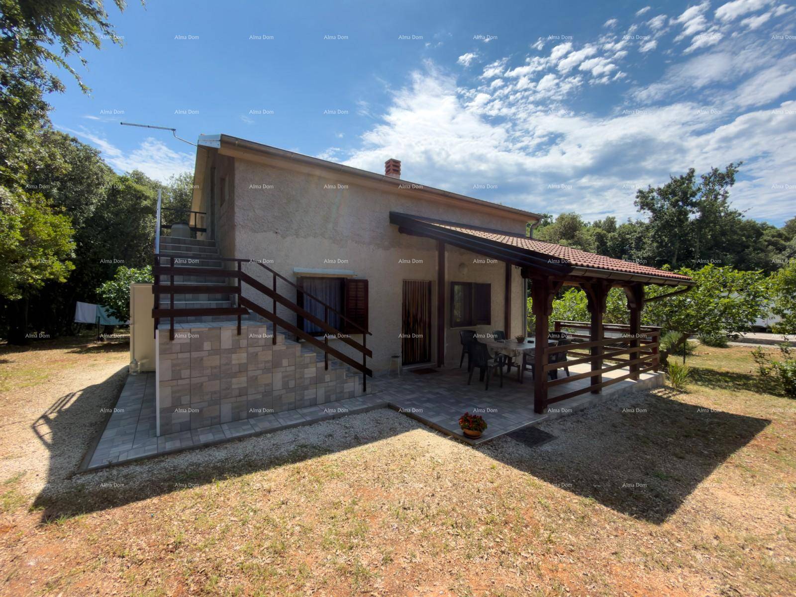Einfaches Landhaus mit überdachter Terrasse und Außentreppe in sonniger Umgebung.