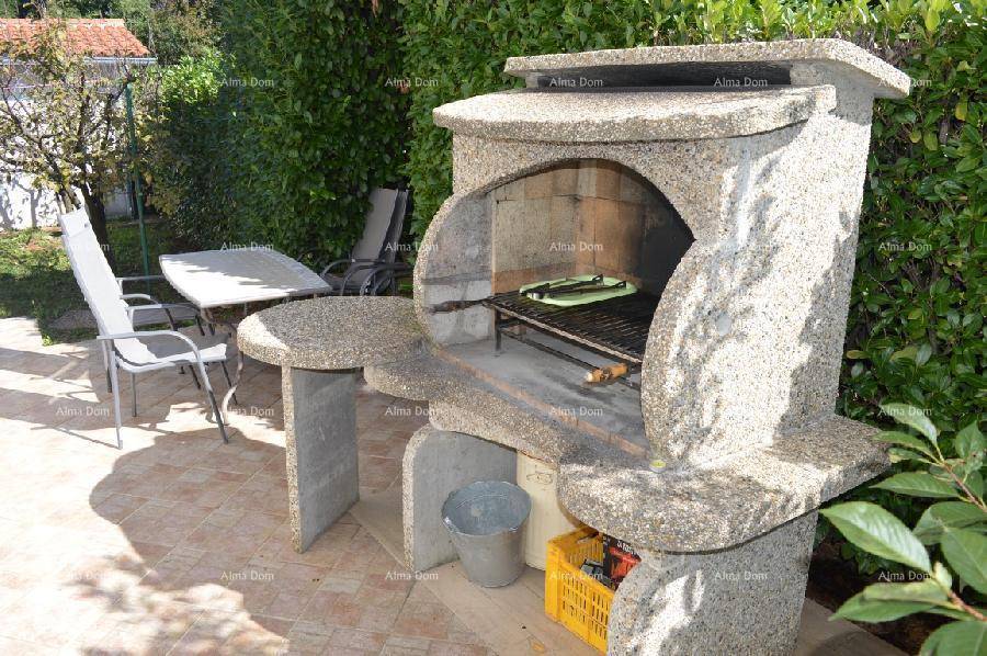 Steingrillbereich mit Esstisch und Stühlen, umgeben von grünen Hecken im Garten an einem sonnigen Tag.
