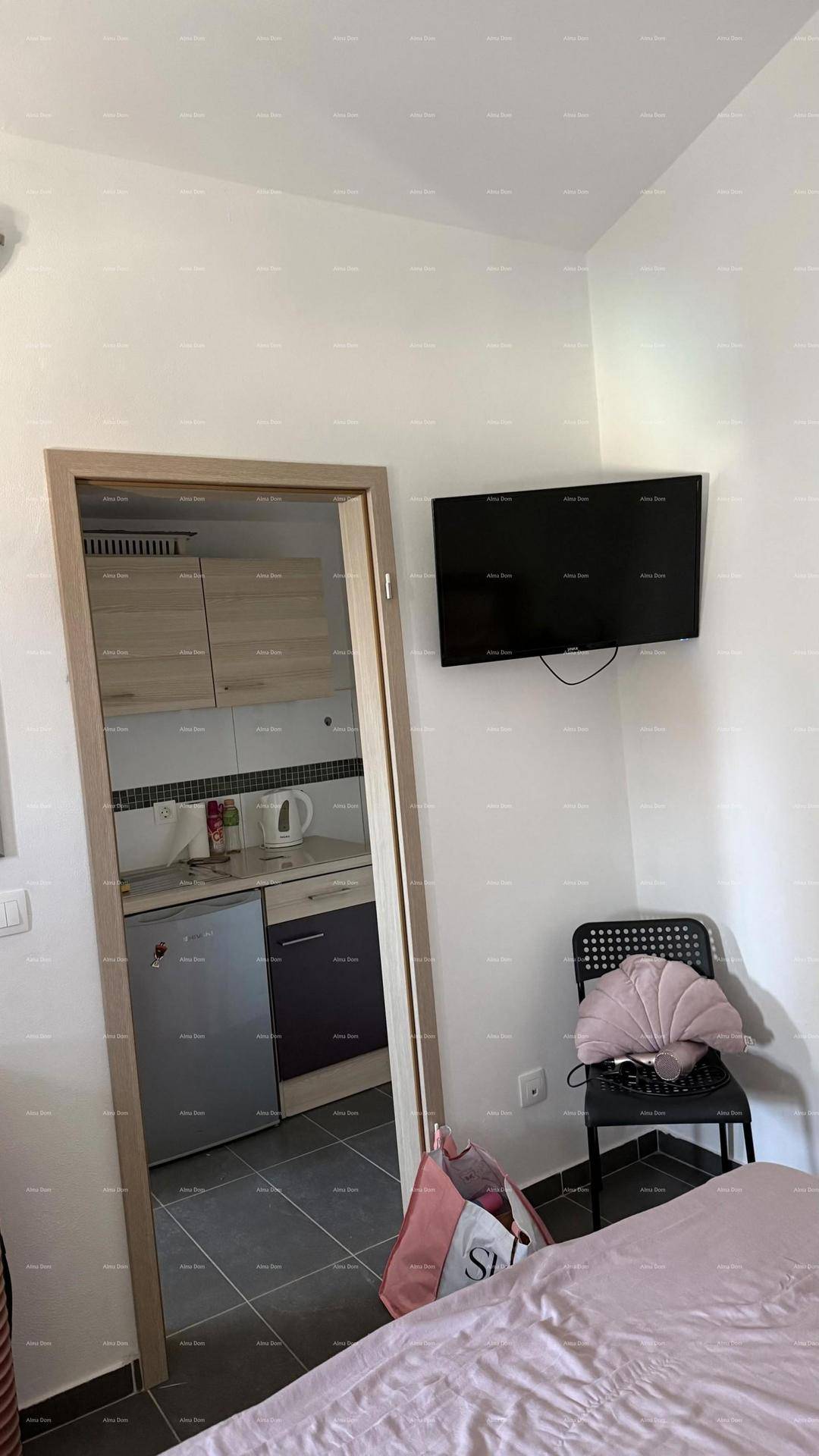 Blick aus dem Schlafzimmer mit Wandfernseher in eine angrenzende kleine Küche.
