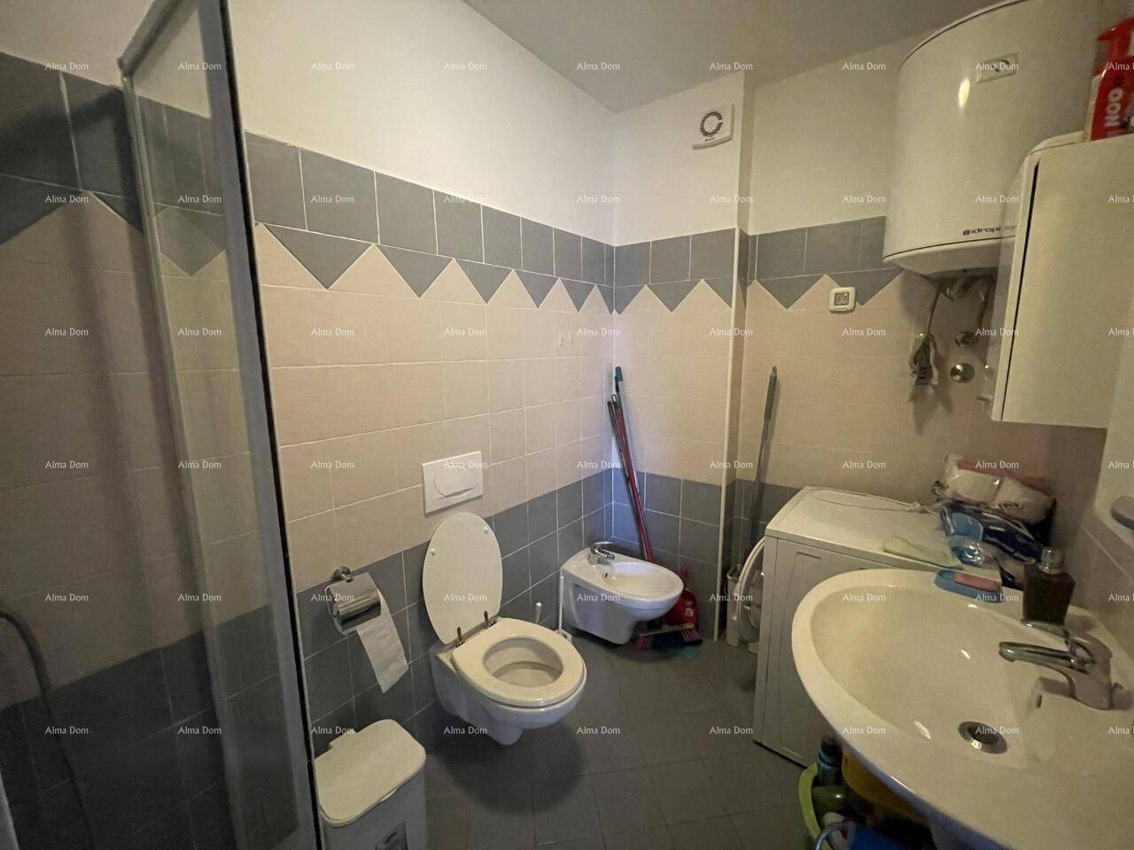 Funktionales Badezimmer mit Dusche, WC, Bidet, Waschbecken und Waschmaschine, gefliest in Grau und Weiß.