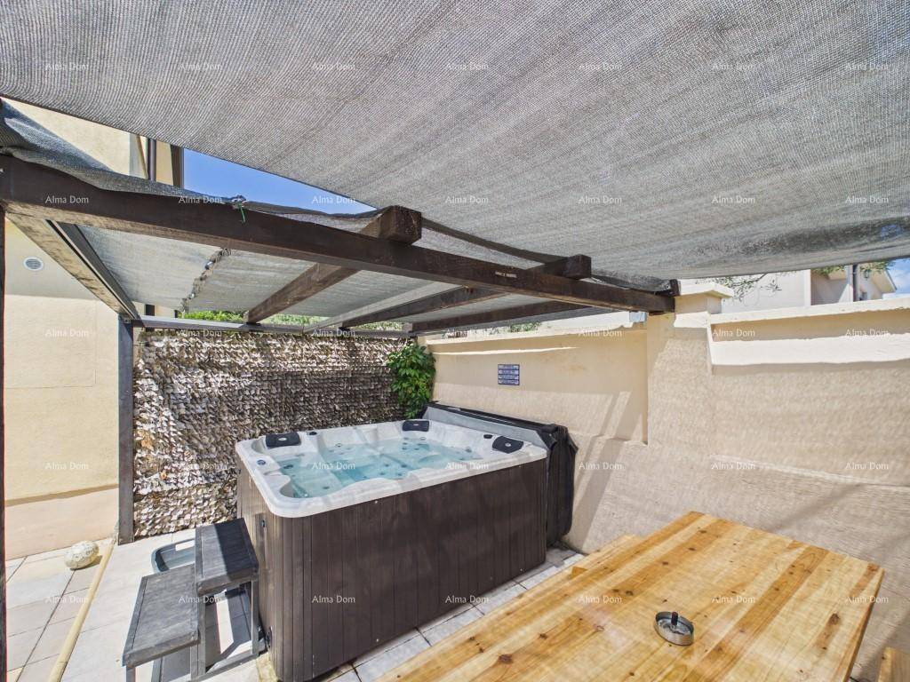 Entspannungsbereich im Freien mit Whirlpool unter einer schattenspendenden Pergola und einem Holztisch.