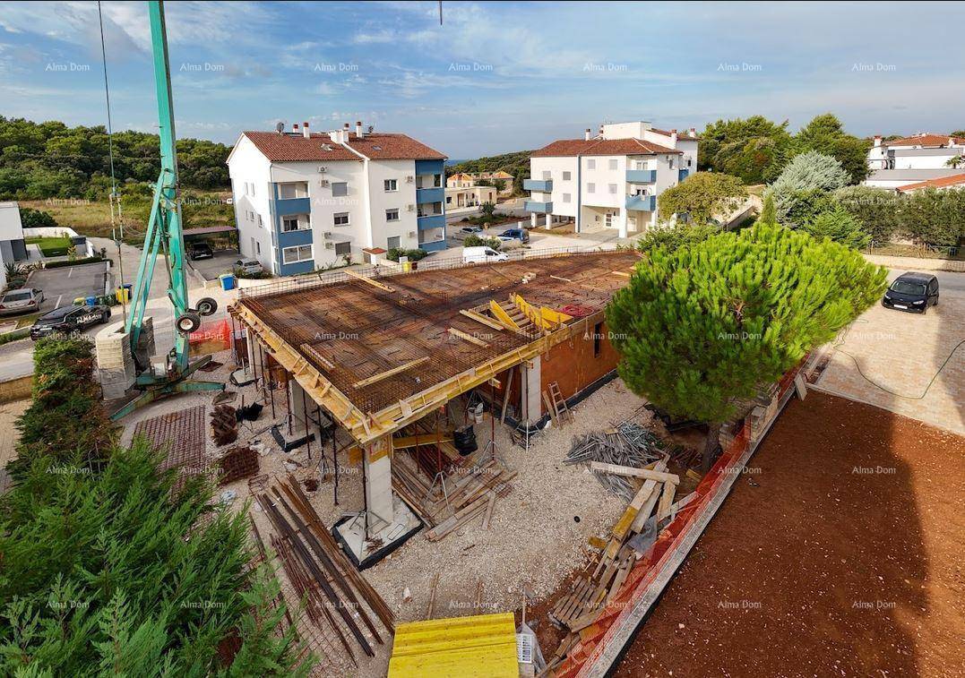 Luftaufnahme einer Baustelle mit Rohbau und umliegenden Wohngebäuden unter blauem Himmel.