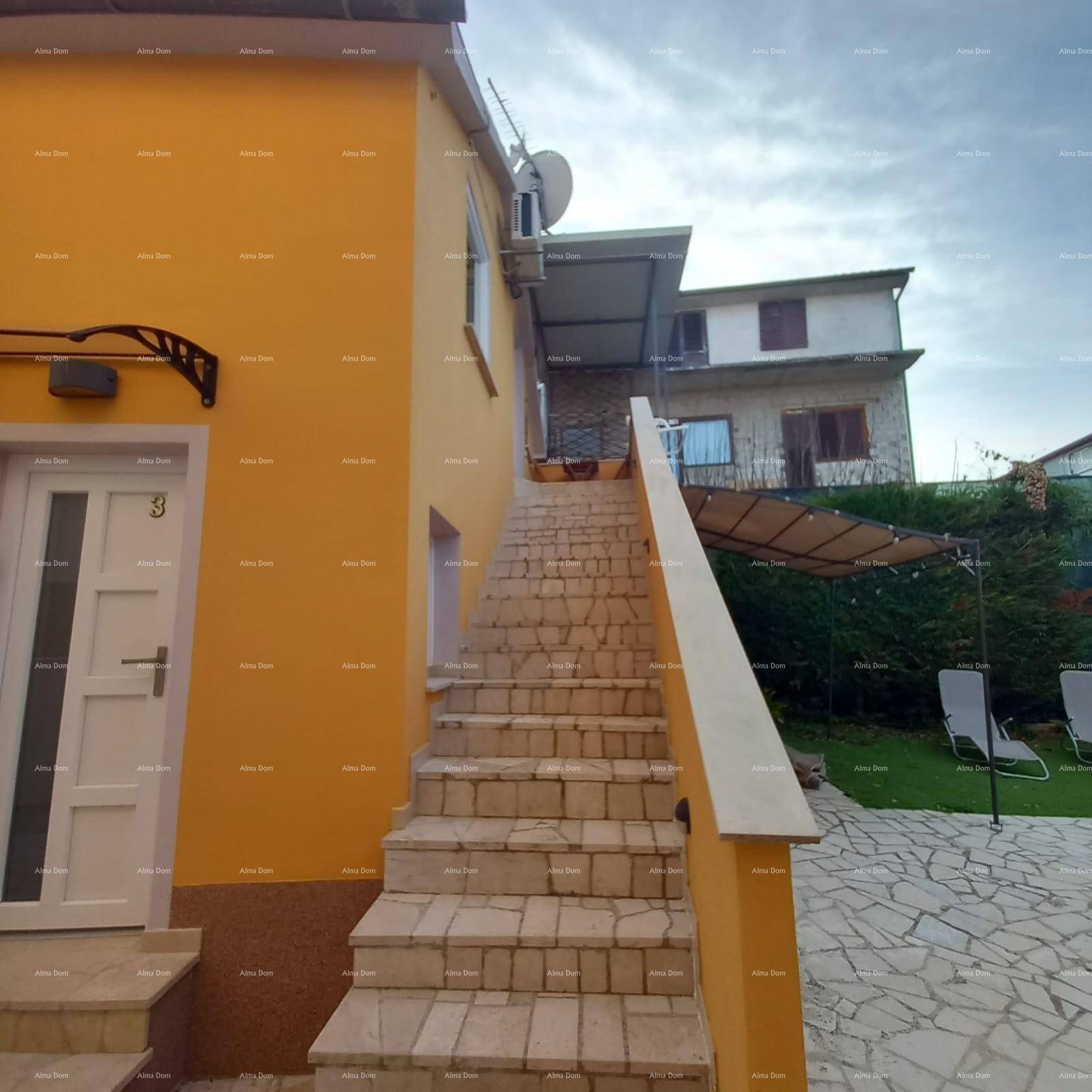 Außenbereich des Hauses mit Steintreppe, gepflastertem Bereich und Garten mit Liegestühlen.