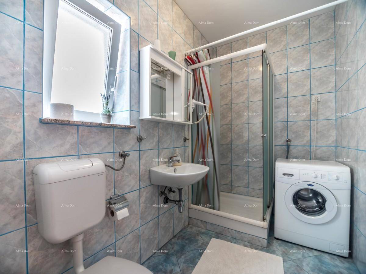 Badezimmer mit blauen Fliesen, Dusche, WC und Waschmaschine, ausgestattet mit einem Fenster.