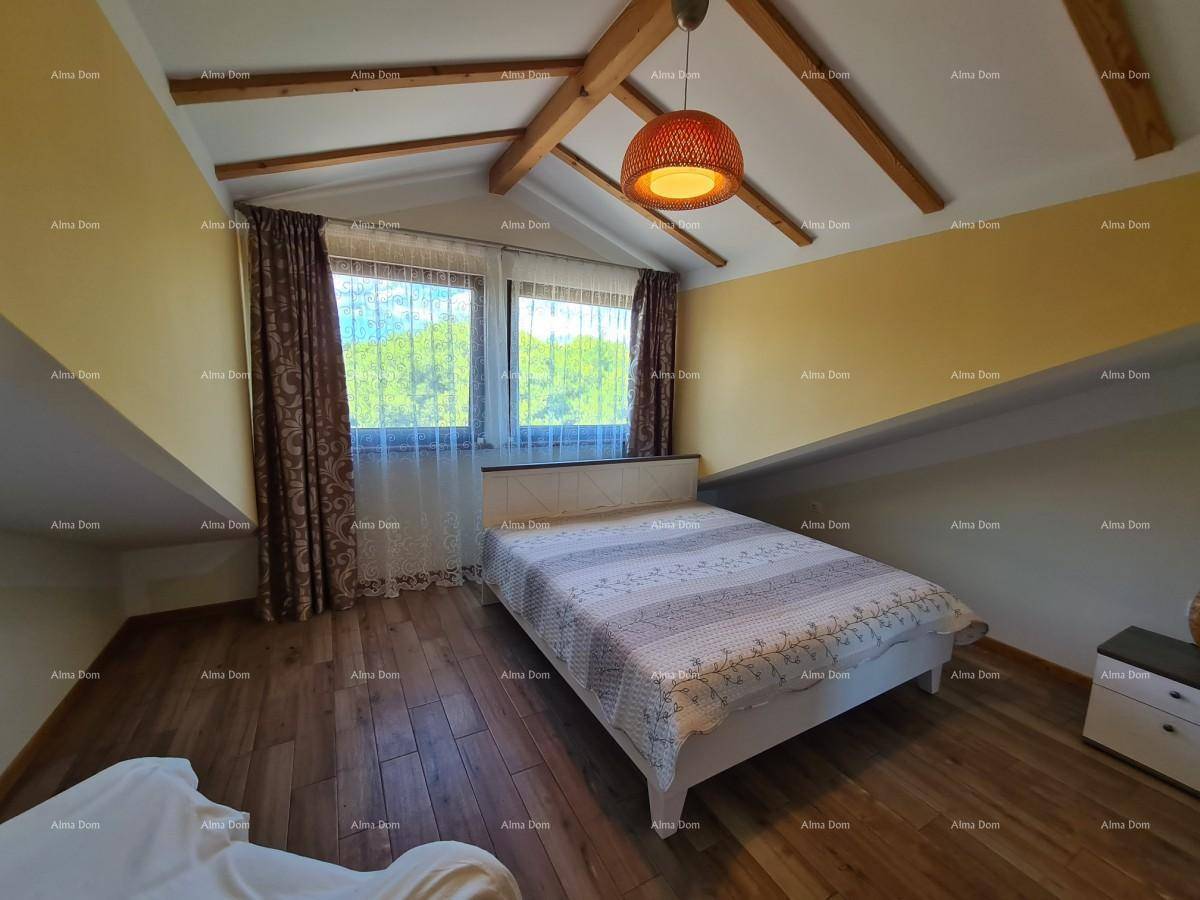 Helles Schlafzimmer im Dachgeschoss mit Holzbalken, schrägen Wänden und großen Fenstern mit Blick ins Grüne.