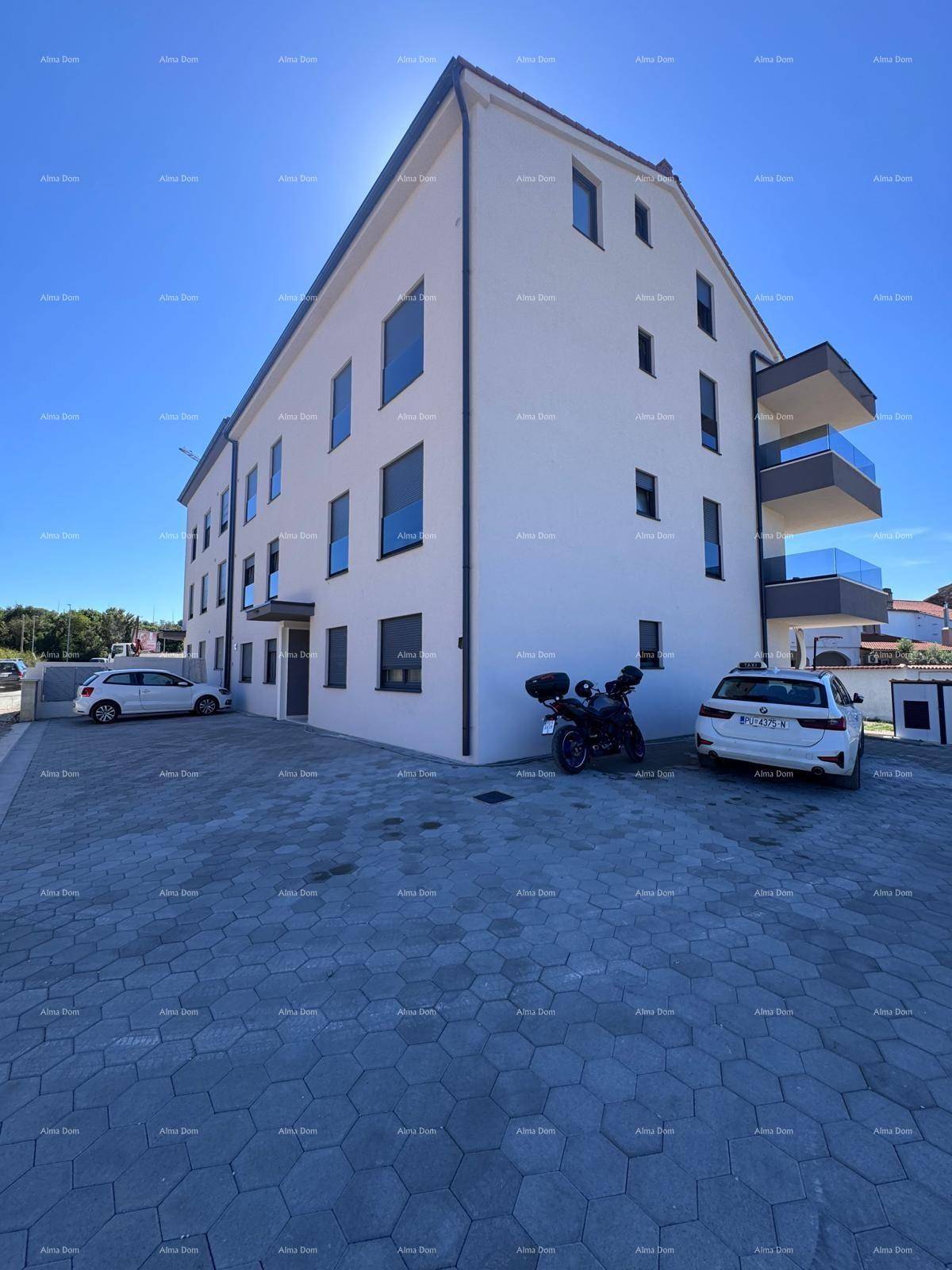 Modernes Mehrfamilienhaus mit Balkonen, heller Fassade und gepflasterten Parkplätzen.