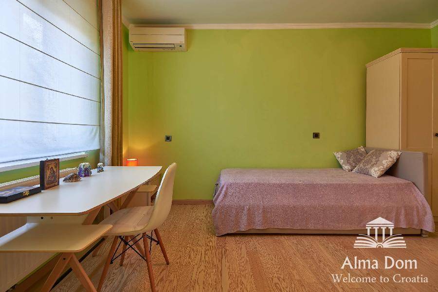 Helles Zimmer mit Schreibtisch, Schlafsofa und grünen Wänden, ideal als Gäste- oder Arbeitszimmer.