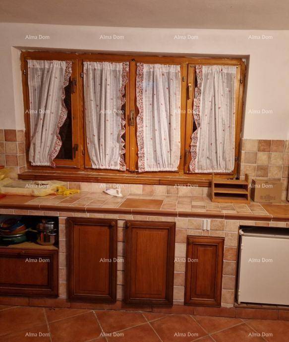 Einfache Küche mit Holzschränken, gefliesten Arbeitsflächen und einem Fenster mit Vorhängen.