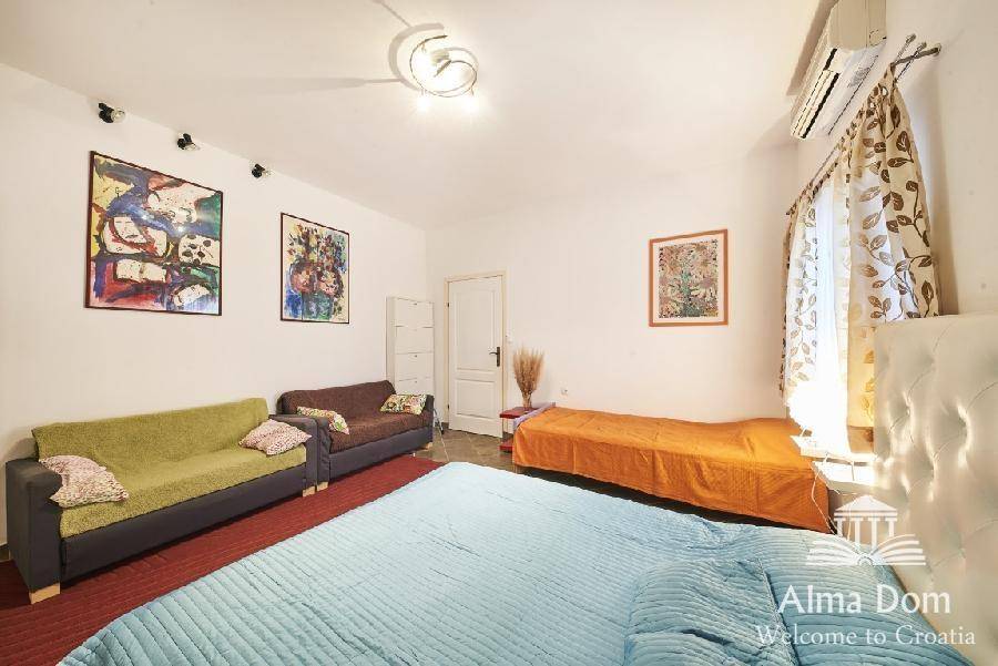 Helles Schlafzimmer mit Doppelbett, Einzelbett, Sofas und farbenfrohen Bildern.