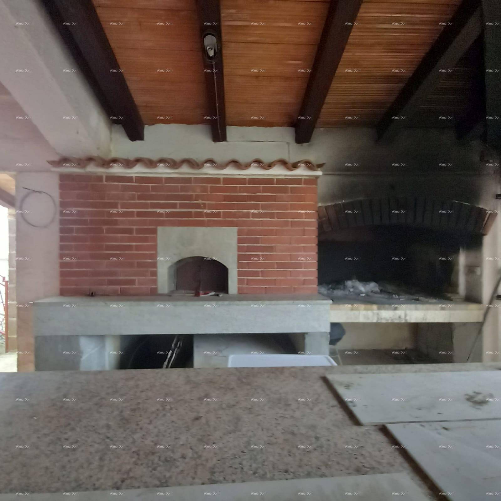 Rustikaler Außenbereich mit gemauertem Pizzaofen und großem Grillplatz unter Holzbalkendecke.