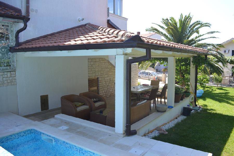 Überdachte Terrasse mit bequemen Rattanmöbeln und direktem Zugang zum sonnigen Poolbereich.