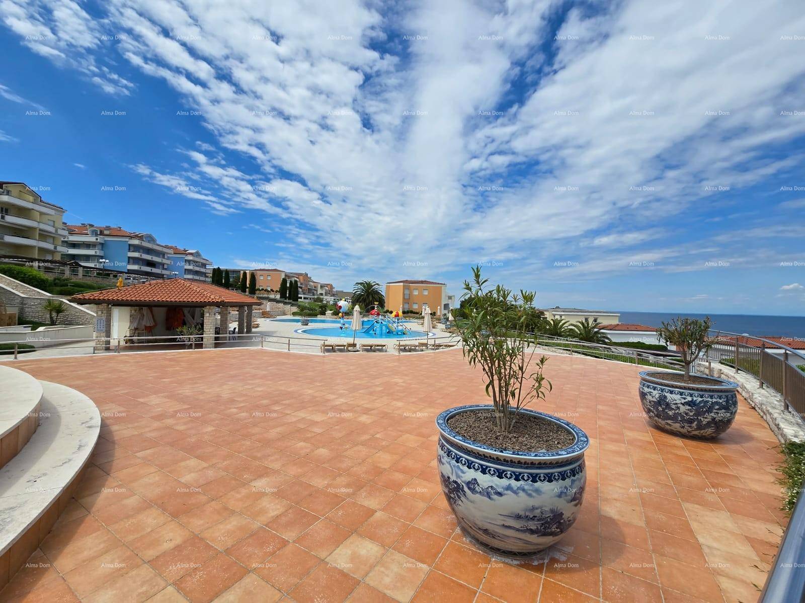 Weitläufige, geflieste Terrasse mit Blick auf die Poolanlage und das Meer unter blauem Himmel.