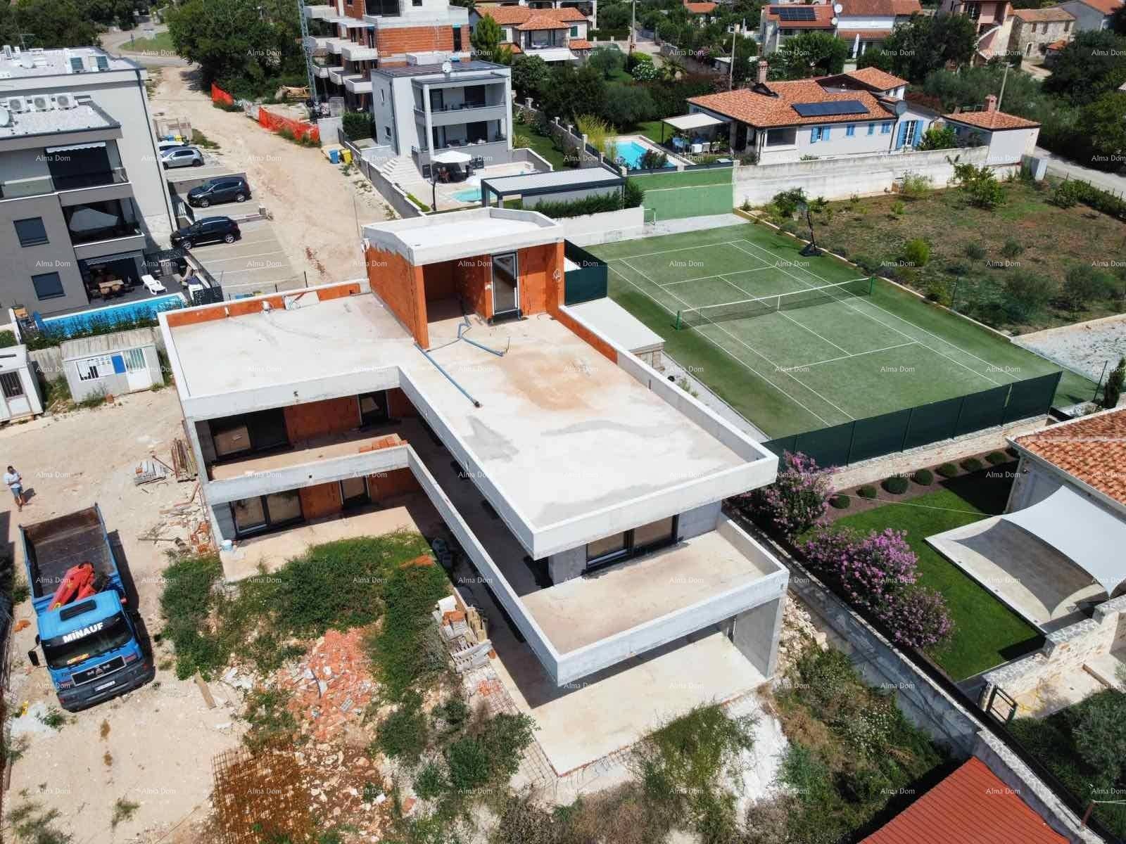 Luftaufnahme eines im Bau befindlichen modernen Hauses mit Flachdächern und Tennisplatz im Hintergrund.