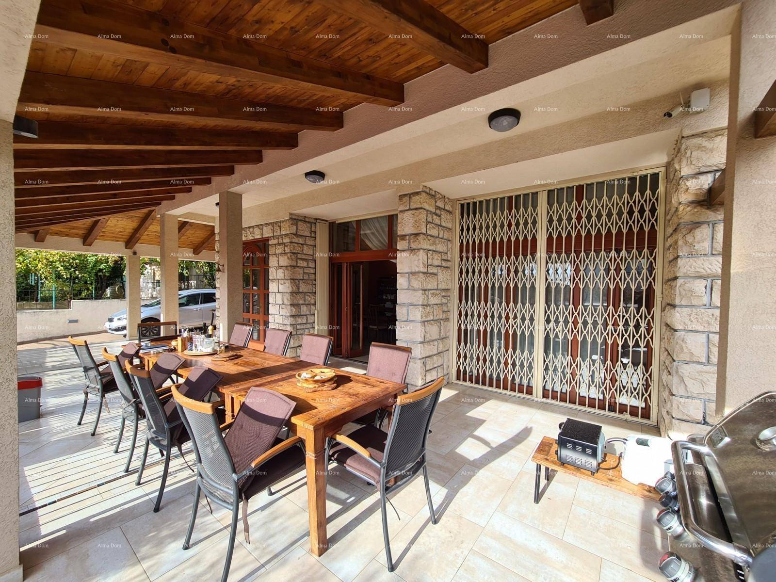 Überdachte Terrasse mit Esstisch und Grill, geschützt durch ein Gittertor.