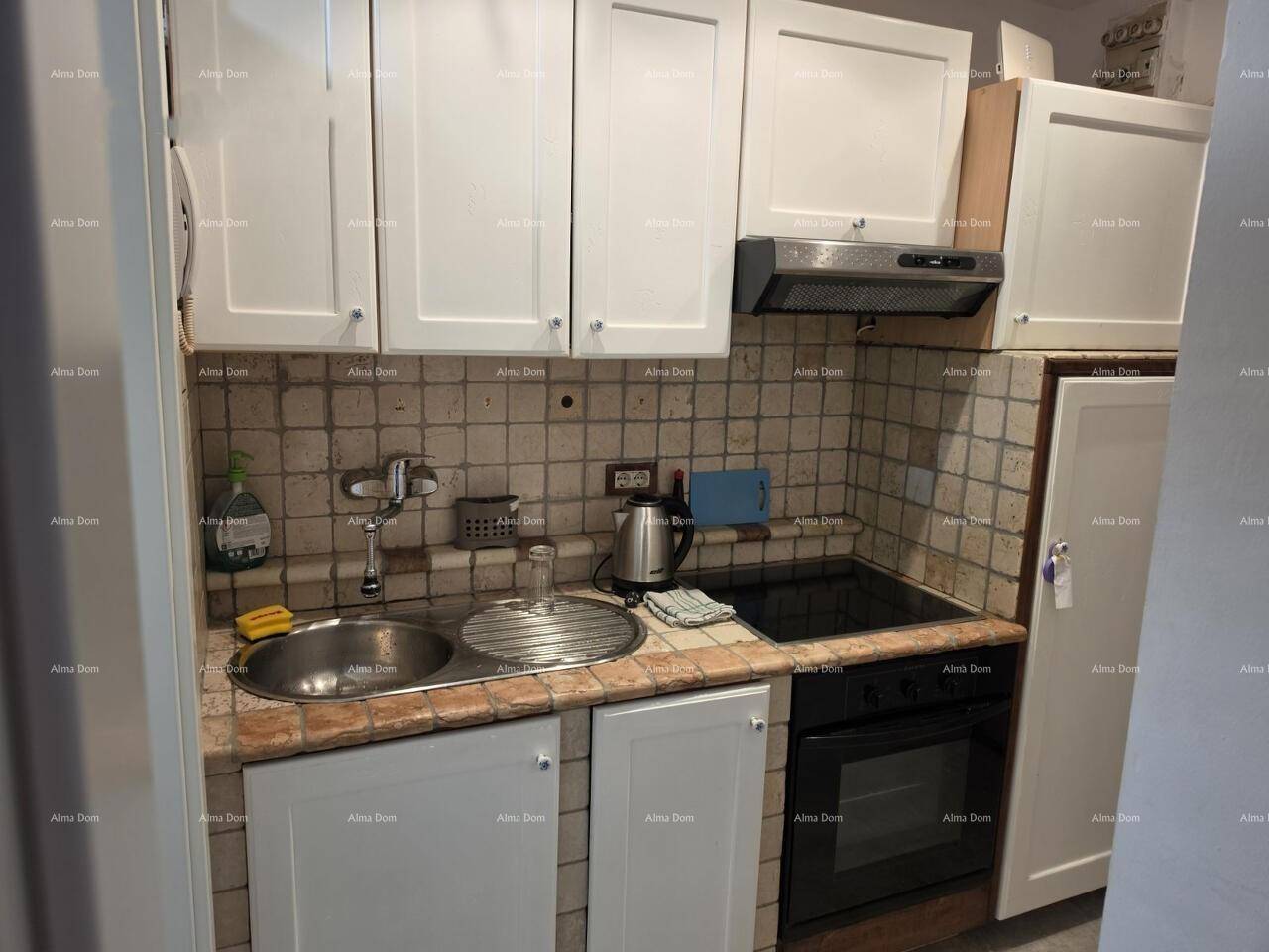 Kleine Küchenzeile mit weißen Schränken, Spüle, Kochfeld und Backofen.
