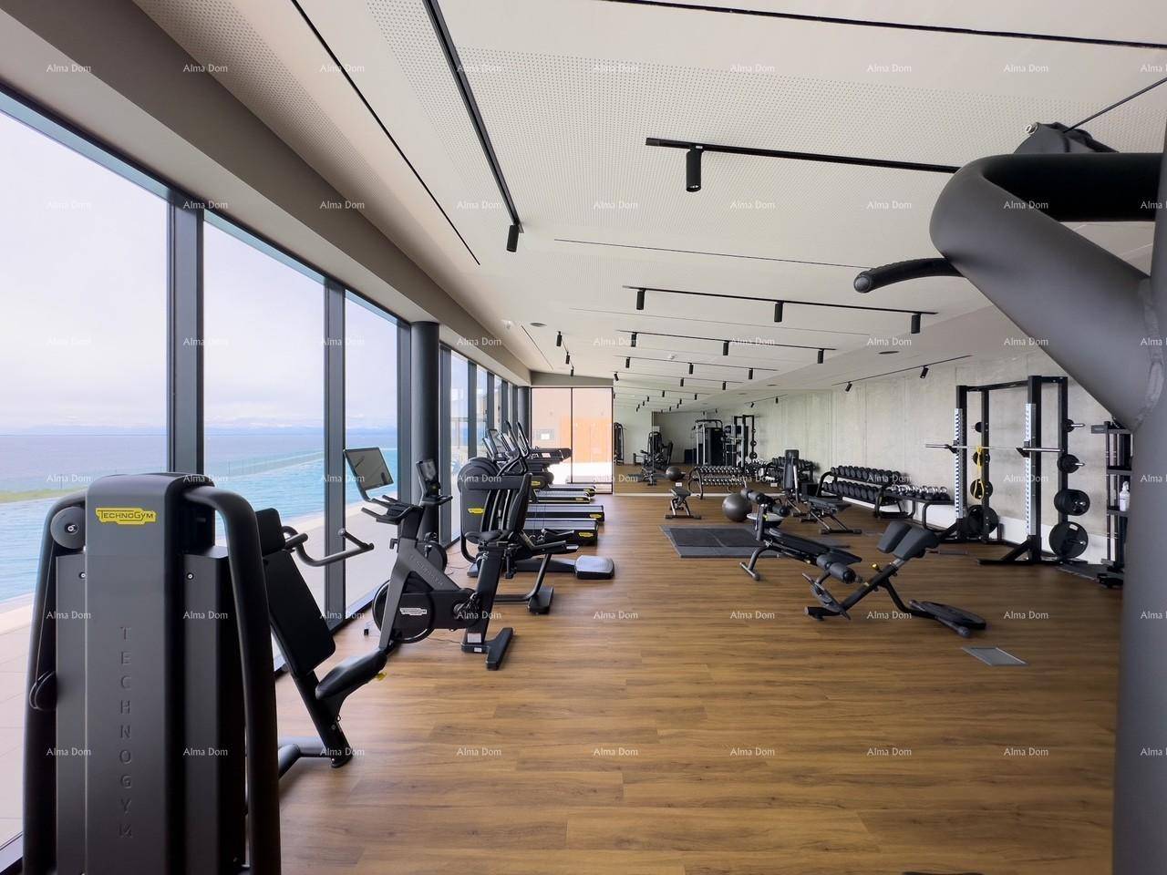 Geräumiges Fitnessstudio mit vielfältigen Trainingsgeräten und Panoramafenstern mit Blick auf das Meer und den Außenpool.