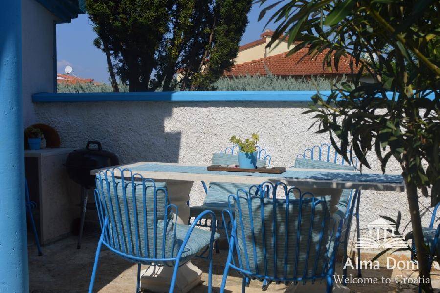Blauer Outdoor-Essbereich mit Grill und Gartenmöbeln unter strahlend blauem Himmel.