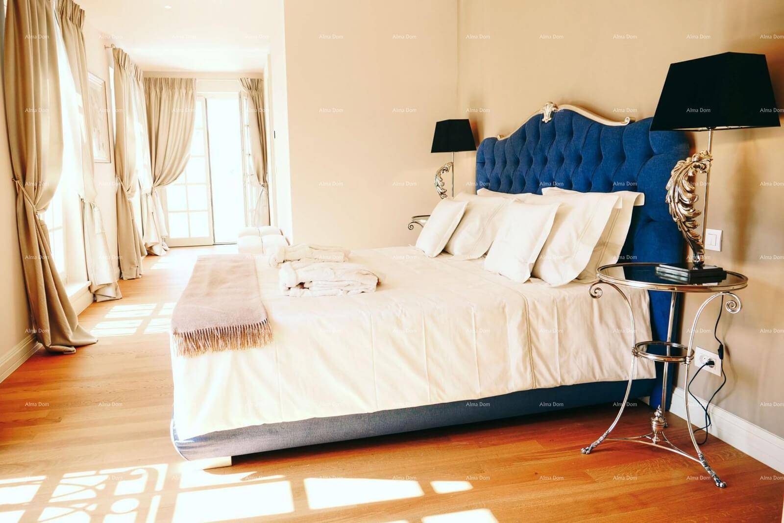 Luxuriöses Schlafzimmer mit blauem, gepolstertem Bett, Holzboden und Balkonzugang.