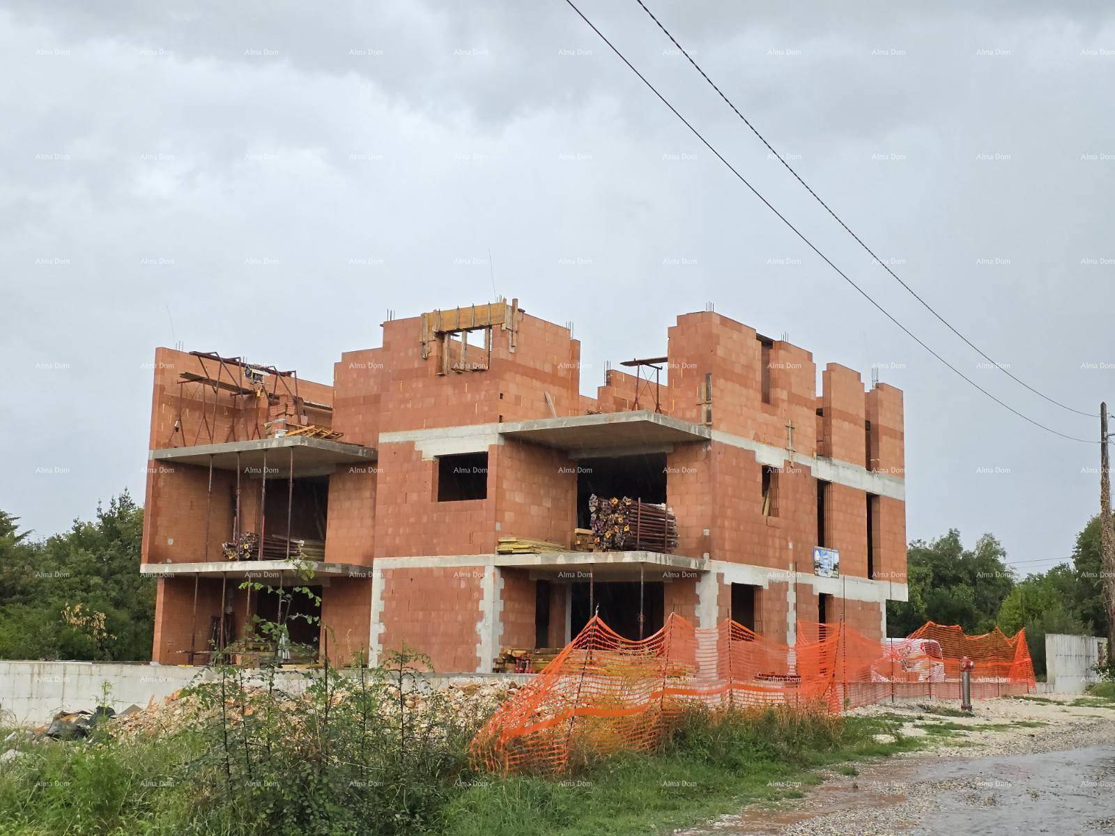 Rohbau eines Mehrfamilienhauses mit Ziegelwänden und sichtbaren Baustrukturen unter bewölktem Himmel.