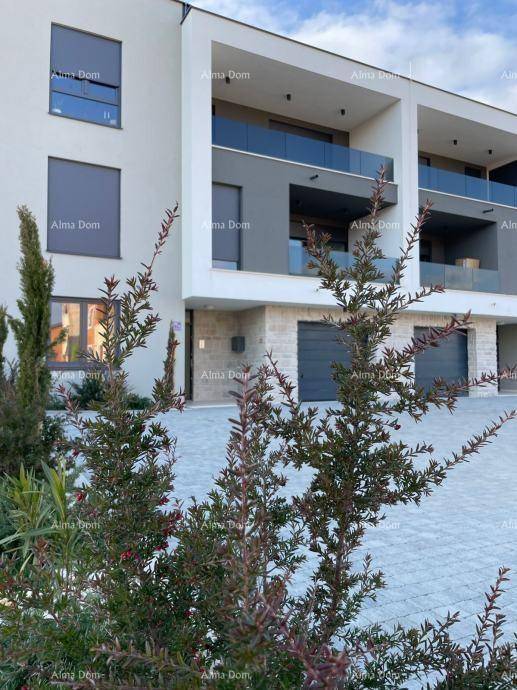 Moderne Gebäudefassade mit Garagenzugang, Balkonen und gepflegter Außenanlage aus Stein.