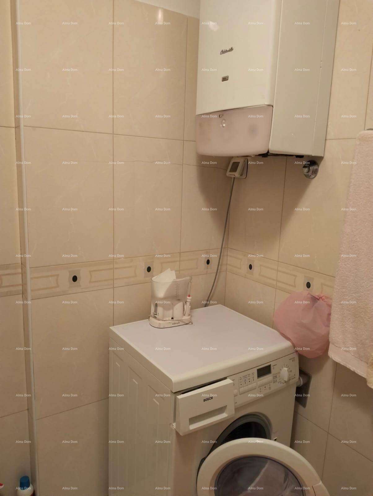 Badezimmerbereich mit Waschmaschine und Warmwasserbereiter, umgeben von hellen Fliesen.