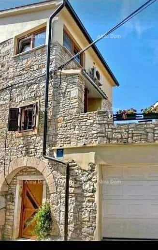 Traditionelles Steinhaus mit Garage und Balkon, umgeben von mediterraner Architektur unter blauem Himmel.