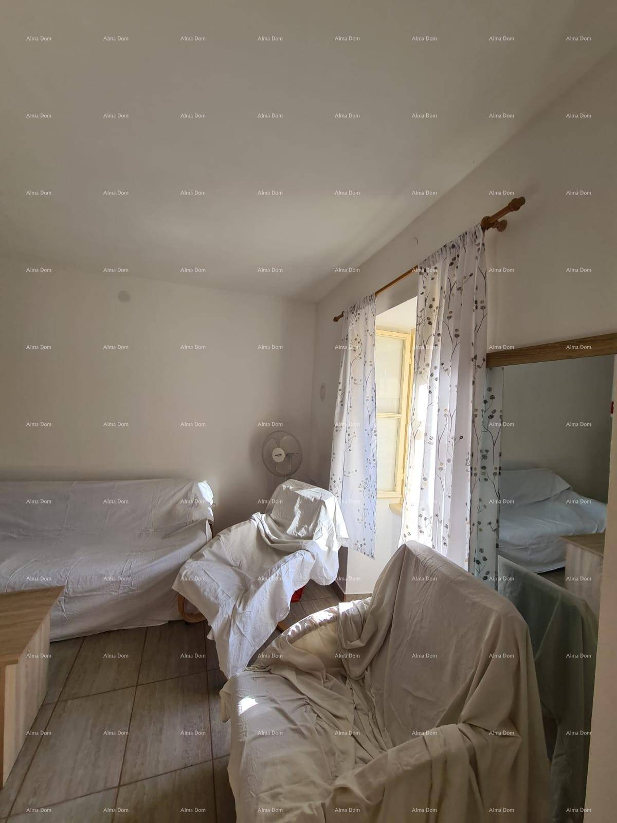 Wohnzimmer mit abgedeckten Möbeln, Fliesenboden und einem Fenster mit hellen Vorhängen.