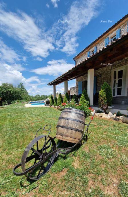 Dekorative Holzfass-Karre im grünen Garten, mit dem Steinhaus und Pool im sonnigen Hintergrund.