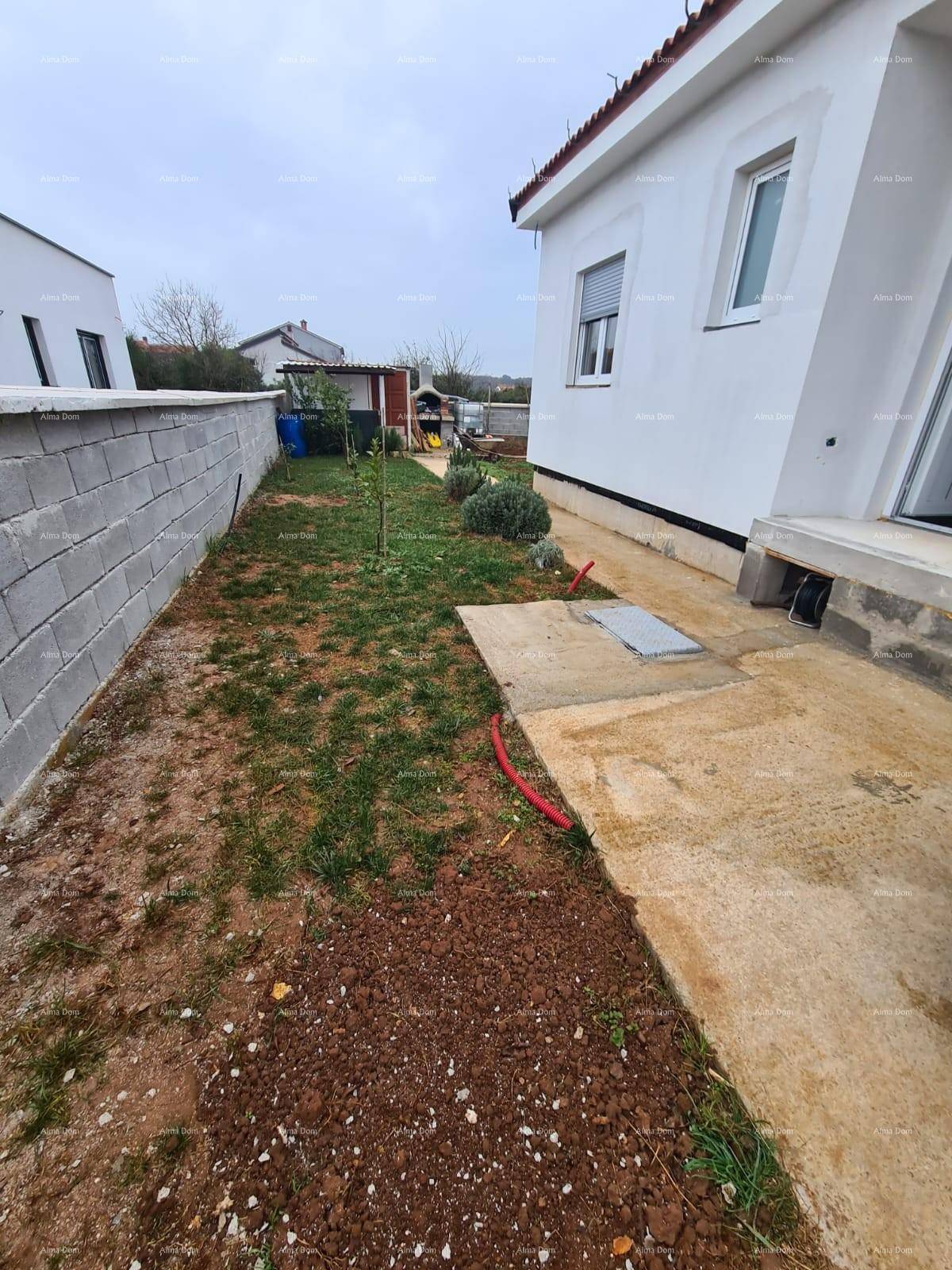 Schmaler Gartenbereich im Bau neben dem Haus mit Betonweg und einer Begrenzungsmauer.
