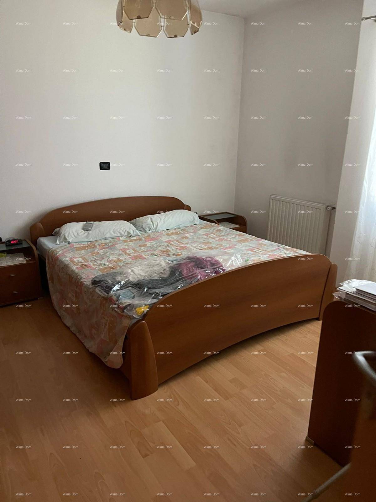Schlafzimmer mit einem großen Doppelbett, hellem Holzfußboden und einem Fenster, das Tageslicht hereinlässt.