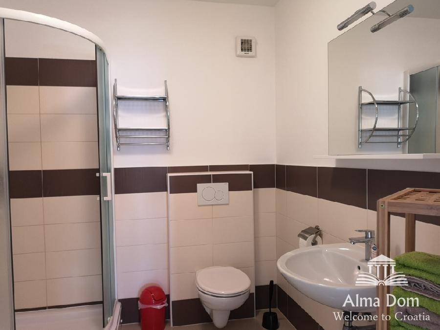 Badezimmer mit Duschkabine, Toilette, Waschbecken und Spiegel, in neutralen Farben gehalten.