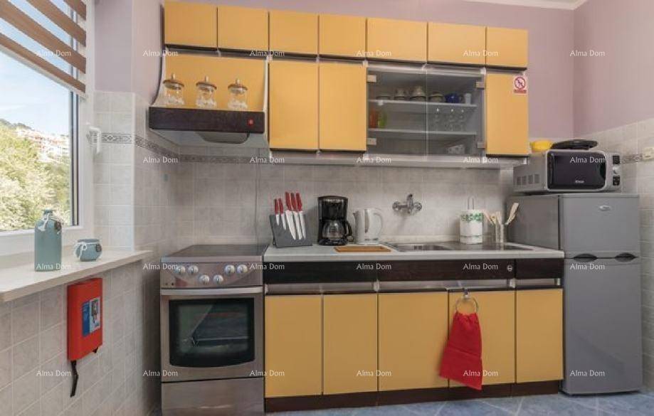 Funktionale Küche mit gelben Schränken, Backofen, Kühlschrank und Fenster mit Blick nach draußen.