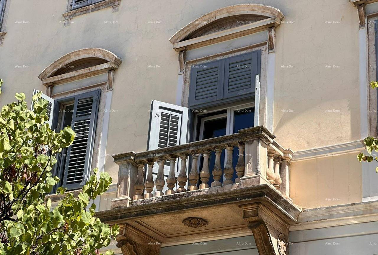 Historische Fassade mit Steinbalkon und Balustrade, ergänzt durch Fenster mit blauen Fensterläden.