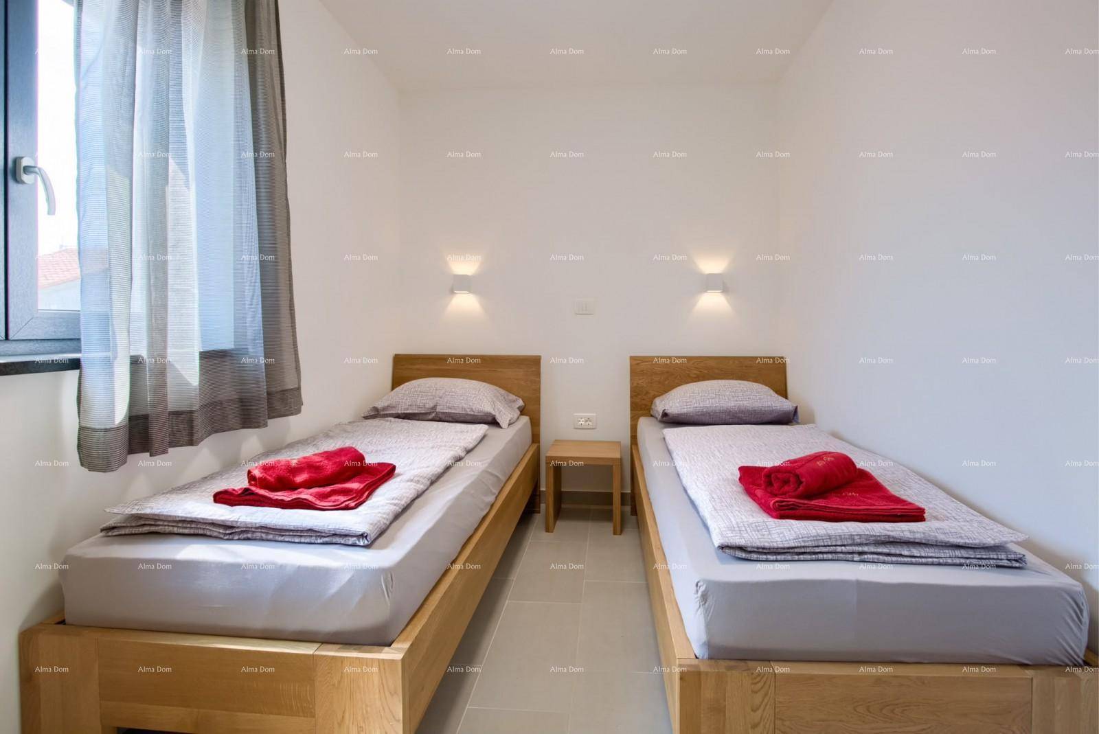 Helles Schlafzimmer mit zwei Einzelbetten aus Holz, grauer Bettwäsche und roten Handtüchern.