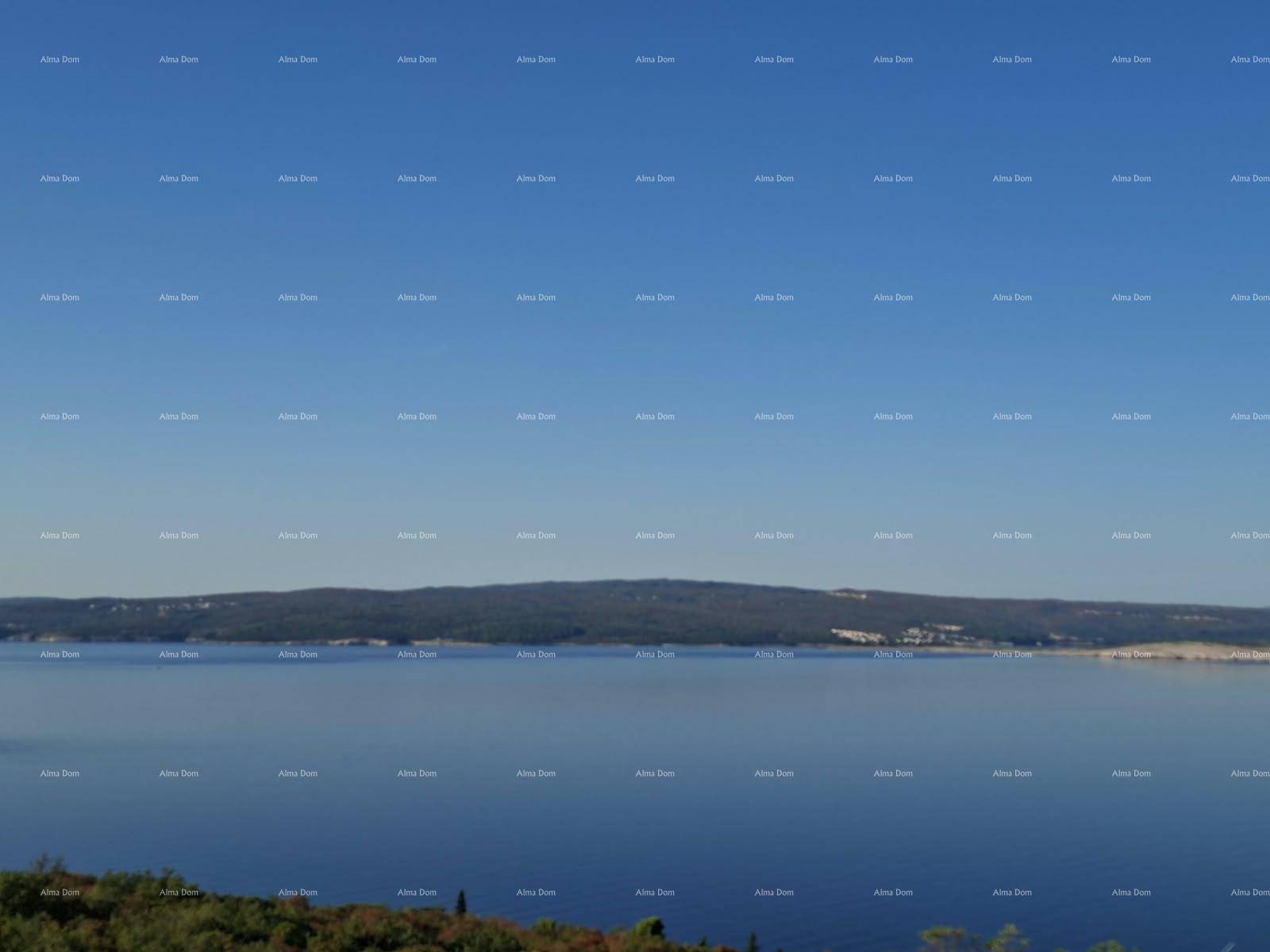 Weitläufiger Panoramablick auf das ruhige Meer und die gegenüberliegende Küstenlinie unter blauem Himmel.