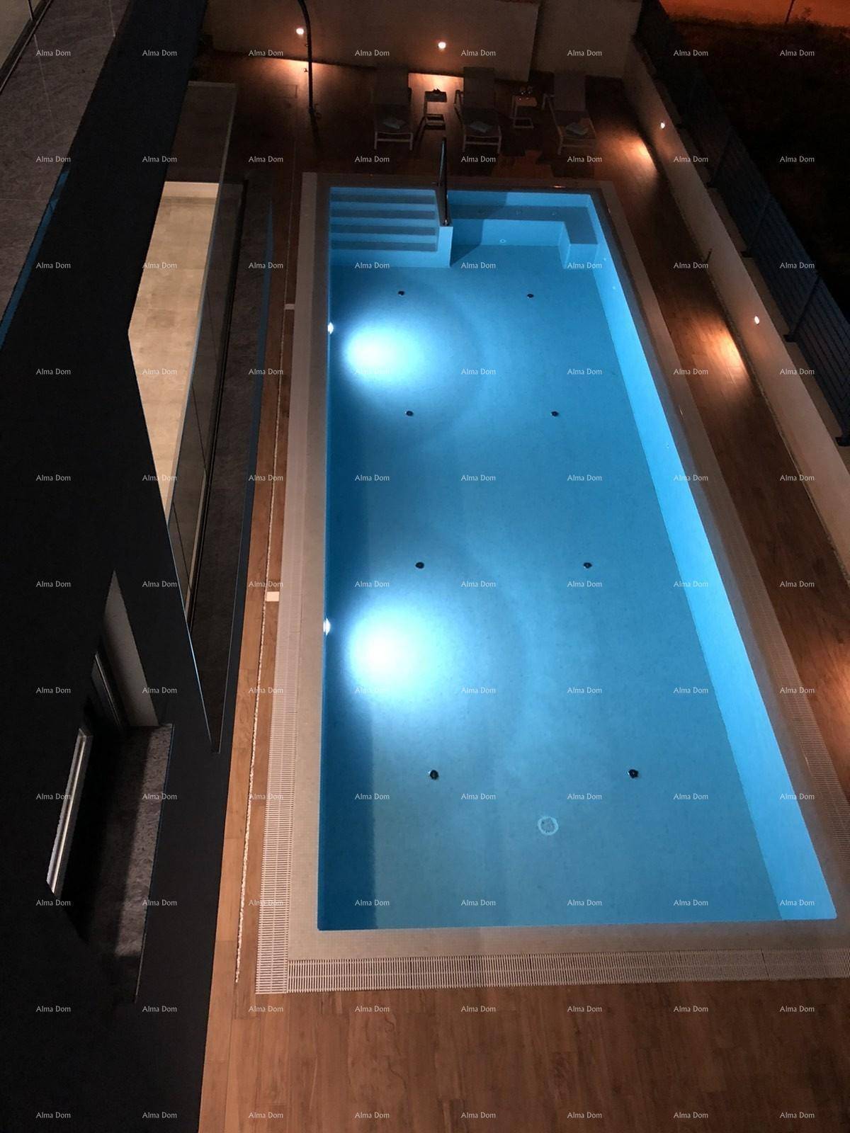 Beleuchteter Außenpool bei Nacht, von oben gesehen, mit Holzdeck und umliegender Beleuchtung.
