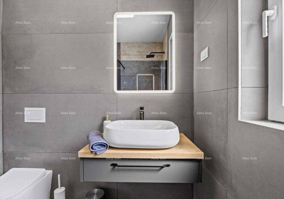 Modernes Badezimmer mit schwebendem Waschtisch, beleuchtetem Spiegel und grauen Fliesen.