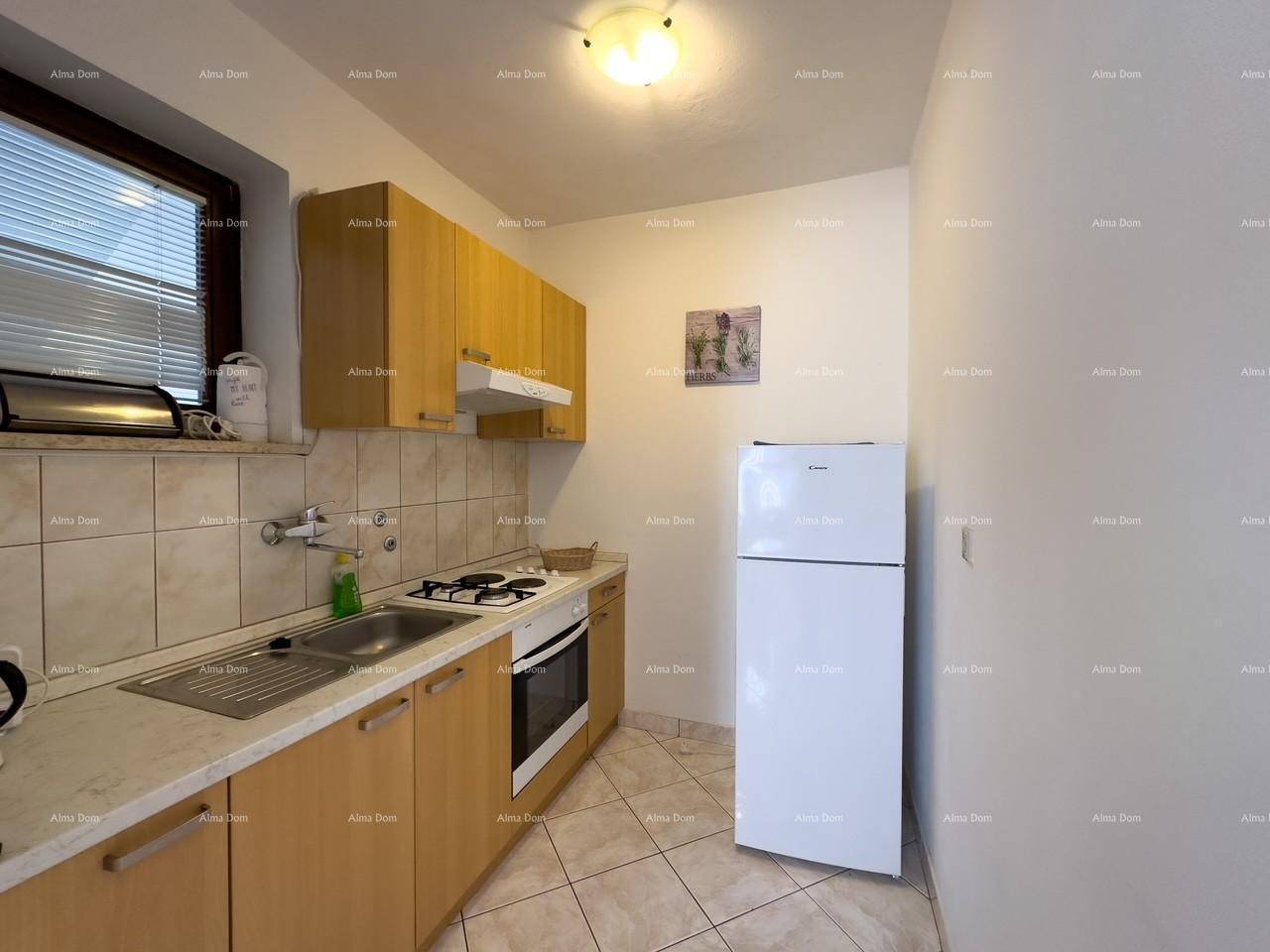 Kleine Küche mit hellen Holzschränken, Kochfeld, Backofen, Spüle und einem weißen Kühlschrank.
